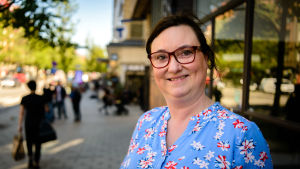 Therese Elias-Gomes beskriver händelsen som ett nationellt trauma. Therese Elias-Gomes är klädd i en blåblommig sommarklänning. Hon har glasögon och ser glad ut.