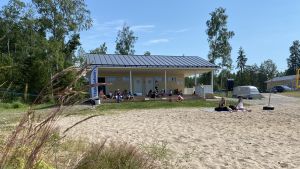Deltagarna i simskolan njuter av mellanmål på trapporna till omklädningsrummen. En gul servicebyggnad med omklädningsrum på en strand.