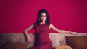 Christine Keeler istuu punaisessa mekossa sohvalla, taustalla punainen seinä.