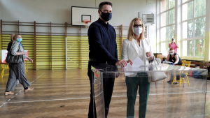Borgmästaren Rafał Trzaskowski och hans fru Malgorzata rlstade på söndagen i staden Rybnik. En man och en kvinna röstar i en gymnastiksal. Båda har munskydd på sig.