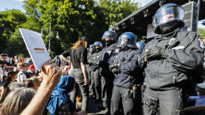 En man håller upp Tysklands grundlag mot kravallpoliser. Poliserna valde senare att skingra demonstranterna, eftersom de inte håll sig till rådande coronaregler. Person håller upp vit bok mot polis i kravallutrustning.