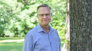 Arkkipiispa Tapio Luoma lähikuvassa kesäisessä maisemassa puun varjossa.