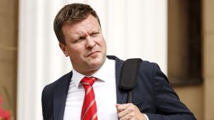 Utvecklings- och utrikeshandelsminister Ville Skinnari (SDP) ska coronatestas efter möjlig exponering för smitta. Minister Ville Skinnari med röd slips och mörkblå kavaj. Han håller i en väskas rem med ena handen och tittar bort från kameran.