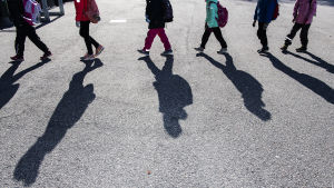 Inger Damlin från Finlands svenska lärarförbund är orolig för att coronakrisen och de ekonomiska problemen den medverkat till ska ha liknande konsekvenser som recessionen under 1990-talet. Arkivbild. Skolelever går i kö med säkerhetsavstånd mellan varandra. De kastar långa skuggor mot asfalten.