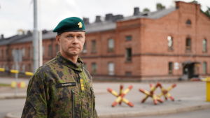 Stabschefen Mika Immonen vid Nylands brigad uppmanar beväringarna att följa myndigheternas råd och rekommendationer så klarar brigaden av coronaviruset. En man i uniform och en namnbricka med namnet Immonen ser allvarligt in i kameran. I bakgrunden ett stort tegelhus i kasernstil.