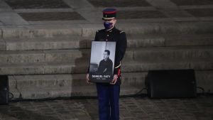 Minnesstunden inleddes med sången ''One'' av bandet U2. Bild på man som håller i stor bild på läraren Samuel Paty.