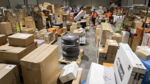 Enligt en undersökning kommer 2,5 miljoner finländare att beställa julklappar via nätet i år. Paljon paketteja hallissa. Työntekijöitä lajittelemassa.