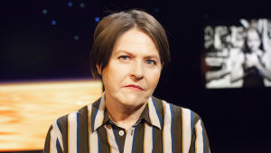 Heidi Hautala gästar Daniel Olin i veckans avsnitt och berättar bland annat om tomheten som hon upplever med distansjobb, då hon saknar att inte kunna träffa sina kollegor i Bryssel. "Jag behöver de informella kaffestunderna." Politiker Heidi Hautala med randig klänning i tv-studion.