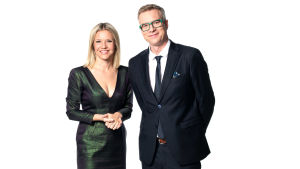 Sonja Kailassaari och Mårten Svartström bjuder in till förfest. En kvinna i en skinande mörkgrön klänning och en man i mörk kostym och gröna glasögonbågar. De ser glada ut.