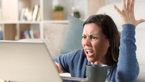 Kuvassa on nainen toinen käsi ylhäällä ja toinen kannettavan tietokoneen näppäimistöllä. Hän näyttää nähän yllättyneeltä ja ärtyneeltä. 