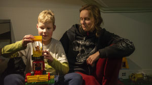 Henna Kapanen vill att Roni bor varannan vecka hos henne. Det växelvisa boendet stöder hela familjens ork och välmående, tycker både hon och hennes exman. Hon efterlyser en förnyelse av lagstiftningen, så att man bättre tar hänsyn till att växelvis boende är vardag för allt fler barn. Pojke och hans mamma sitter tillsammans. Pojken roar sig med leksakstraktor.