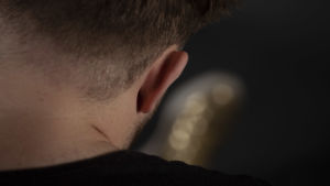 Blir man lyckligare av att sjunga i kör, eller är det bara lyckliga människor som vill vara med i körer? Jonas nacke och ena öra fotograferat bakifrån, med hans guldfärgade sko suddig i förgrunden.