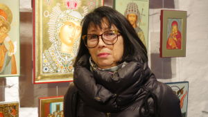 Erna Lorech-Reponen började måla ikoner för tolv år sedan. En mörkhårig kvinna i dunjacka och stora glasögon står framför en vägg med ikoner.