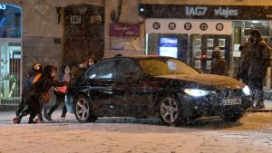 Spanjorerna uppmanas undvika onödiga bilresor. Människor skjuter på en bil på en snöig stadsgata.