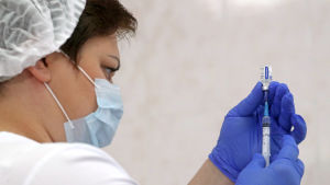 Enligt en opinionsundersökning säger 58 procent av ryssarna att de inte vill ta coronavaccinet. En kvinna i munskydd, hårskydd samt blå plasthandskar fylker en spruta med vaccin.