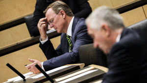 Delstaten Thüringens regeringschef Bodo Ramelow hör till dem som vill att delstatsparlamenten ska få mer makt. En man i svart kostym och vit skjorta ser ner på sin telefon. Han bär en gul- och svartrandig slips och diskreta glasögon. Han tar sig för pannan med högerhanden. I förgrunden syns en annan man men han är inte i fokus.