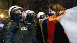 Flera greps av polis i samband med protesterna. En kvinna håller upp ett plakat framför poliser i Polen.