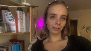 Julia är oftast hemma i sin lägenhet eftersom alla studier sker på distans. En kvinna med kort blont hår. Hon står i en lägenhet, framför en bokhylla.