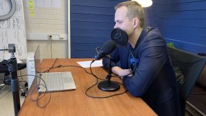 Webinar gör det möjligt att hjälpa kunder runt om i världen. En man i kavaj sitter vid en mikrofon vid daton vid ett skrivbord.