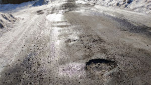 En grop i vägen i korsningen mellan Gamla Kungsvägen och Riddarbågen i Borgå. En stor grop mitt i en asfaltväg som har rejält med sand och smält snö på sig.