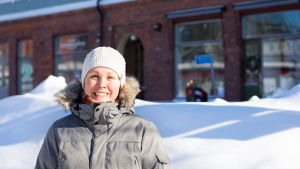Sanna Päivärinta. En kvinna står ute i soligt vinterväder och ler in i kameran.