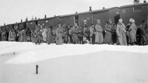 Flyktingar lastas på tåg i Terijoki. Svartvit bild från 1921. Människor i vinterkläder står i snön intill ett tåg. Flyktingar lastas på tåg i Terijoki.