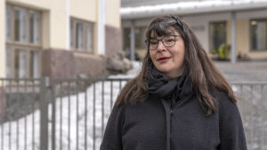 Pia Tyyskä är uppvuxen i Helsingfors men har bott i Lahtis sedan slutet av 1990-talet. Hon vill göra sitt modersmål mera synligt i sin hemstad. Pia Tyyskä står framför ett metallstaket.