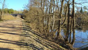 En paviljong planeras invid Pyttisgrenen av Kymmene älv. Sandväg, en älv till höger täckt av träd, längst fram skymtar en motorvägsbro i betong.
