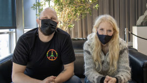 Paleface ja Susan Aho istuvat sohvalla vierekkäin maskit päällä.