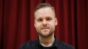 Närpes teaters ordförande Simon Nystén säger att de utgår från att kunna spela teater i sommar. Mansperson står på teaterscen, i bakgrunden rött sammetsdraperi.