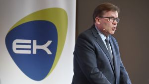 Keskos vd Mikko Helander är ordförande för EK:s arbetsgrupp. En man i mörk kostym med kort hår och glasögon står lite framåtlutad och pratar. Han har en liten mikrofon vid sin kind. Den är fäst med en tråd över örat. I bakgrunden en skylt som det står EK på och runt texten en ram i grönt och blått.