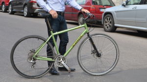 En grön cykel. En man håller i cykeln, endast hans nedre kropp syns i bild.