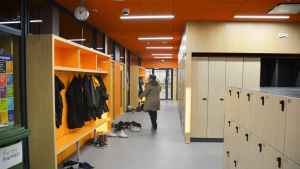 Skolkorridoren är orange. Bakom finns matsalen, där både finska och svenska elever rör sig. orange skolkorridor, lärare går i korridoren