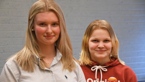 Emma Hansson och Malin Lindfors studerar till närvårdare. Två elever står och ler bredvid varandra i sitt klassrum i Prakticum.