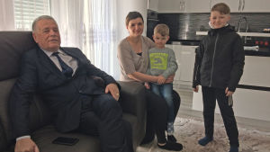 Agim Hasani är kommunordförande i Chabra. Hans svärdotter Lumturie bor i Vasa och är på besök med sin familj. Man sitter på en soffa, bredvid soffan sitter en kvinna med en pojke i famnen. Bredvid kvinnan står en litet äldre pojke. I bakgrunden syns ett kök.
