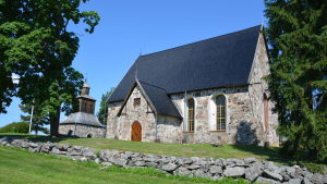 En bild av hela den gamla kyrkan med stenmur framför. 