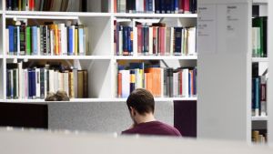 En studerande i Helsingfors universitets huvudbibliotek sitter med hörlurar i öronen och med ryggen vänd mot kameran.