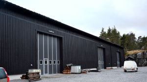 Båtförvaringshallen står klar och är fullastad med övervintrande båtar. Baggö Marinas båtförvaringshall, en stor, svart byggnad i trä.