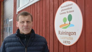 Juha Raininko. Juha Raininko bredvid en skylt för ekogården Rainingon luomutila.