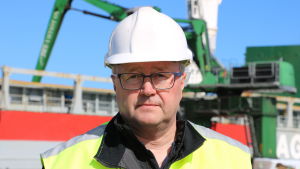 Ilkka Hovi. En man med glasögon och skyddshjälm på huvudet står framför ett fartyg.