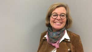 Service på svenska står Wiveka Kauppila nära hjärtat. wiveka kauppla leende mot kameran iklädd brun jacka mot en grå bakgrund.