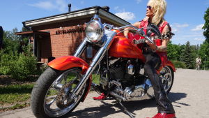 Michael Monroe blev redan förtjust i Karis. Här poserar han på en Karisbos motorcyckel. En man i röd läderväst sitter på en röd motorcykel och ler.
