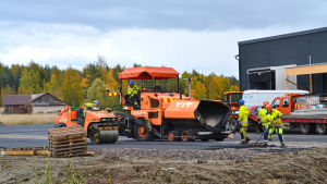 Vägarbetare som jobbar med att asfaltera den blivande parkeringsplatsen vid Borgå potatis nya lokal. En av dem har till och med tid att posera framför kameran. Gatuarbetare som asfalterar parkeringsplatsen.