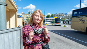 Rosanna Halttunen tycker det är viktigt att använda munskydd i bussen. En kvinna som håller upp ett munskydd.