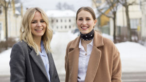 Tänk kvalitet och plagg du länge kommer att tycka om. Då har du en hållbar garderob. Två kvinnor står ute på en gata. Michelle till vänster i bild har långt blont hår och grå kappa. Sandra till höger har håret i hästsvans och beige kappa. Båda ler.