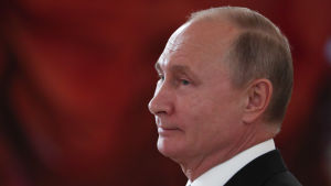 Vladimir Putin. Vladimir Putin i profil mot ett rött draperi i bakgrunden.