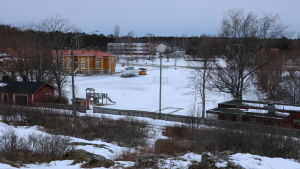 Här mellan Kristinestads skola (till vänster) och det gamla daghemmet ska ett nytt daghem snart byggas. En snöbeklädd miljö. Till vänster i bild en gul trähusbyggnad. Till höger i bild en röd låg byggnad. Mittemellan en öppning.