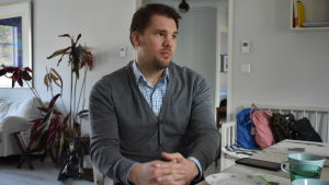 Christopher Lignell är trött på att det inte finns någon långsiktig plan. Man i grå tröja och rutig skjorta sitter vid ett bord med händerna knäppta i knät.