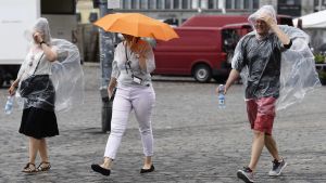 Det blir en svalare och regnigare vecka. Tre personer går ute i regnet i Helsingfors. Två av dem bär en engångsregnjacka och en av dem går under ett paraply.