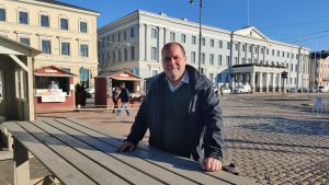 Helsingfors evenemangsstiftelse ordnar det kinesiska nyåret. Stuba Nikula är stitelsens vd. En man står och lutar mot ett trädbord på ett torg.